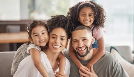 Happy, smile and portrait of an interracial family sitting on a sofa in the living room at home. Happiness, love and adoptive parents bonding, embracing and relaxing with their children in the lounge