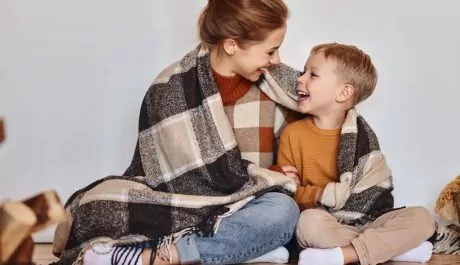 happy family mother and loving son hug and laugh wrapped in a warm blanket on evening at home